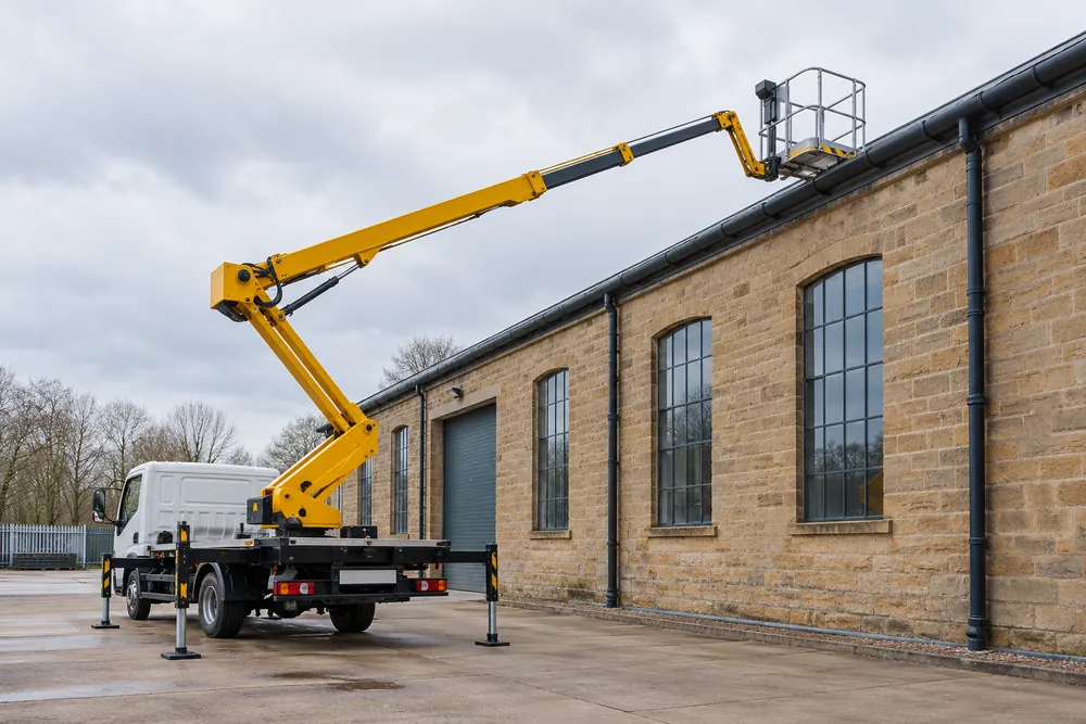Truck-mounted cherry picker with stabilisers deployed beside a warehouse